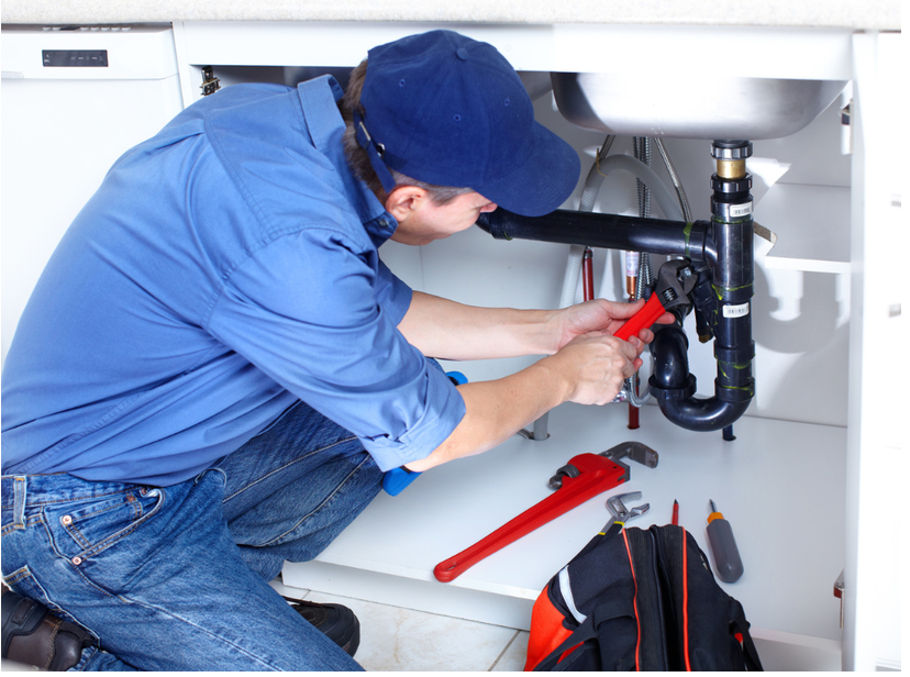 Plumber repairing drain pipes beneath a kitchen sink